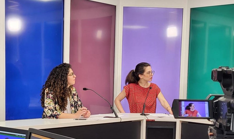 Maya Hagege et Judith Aquien sur un plateau TV. Elles sont installées derrière un pupitre noir et blanc, micro devant elles. Elles regardent vers la droite de l'image. Au premier plan, une caméra est en train de filmer la scène.