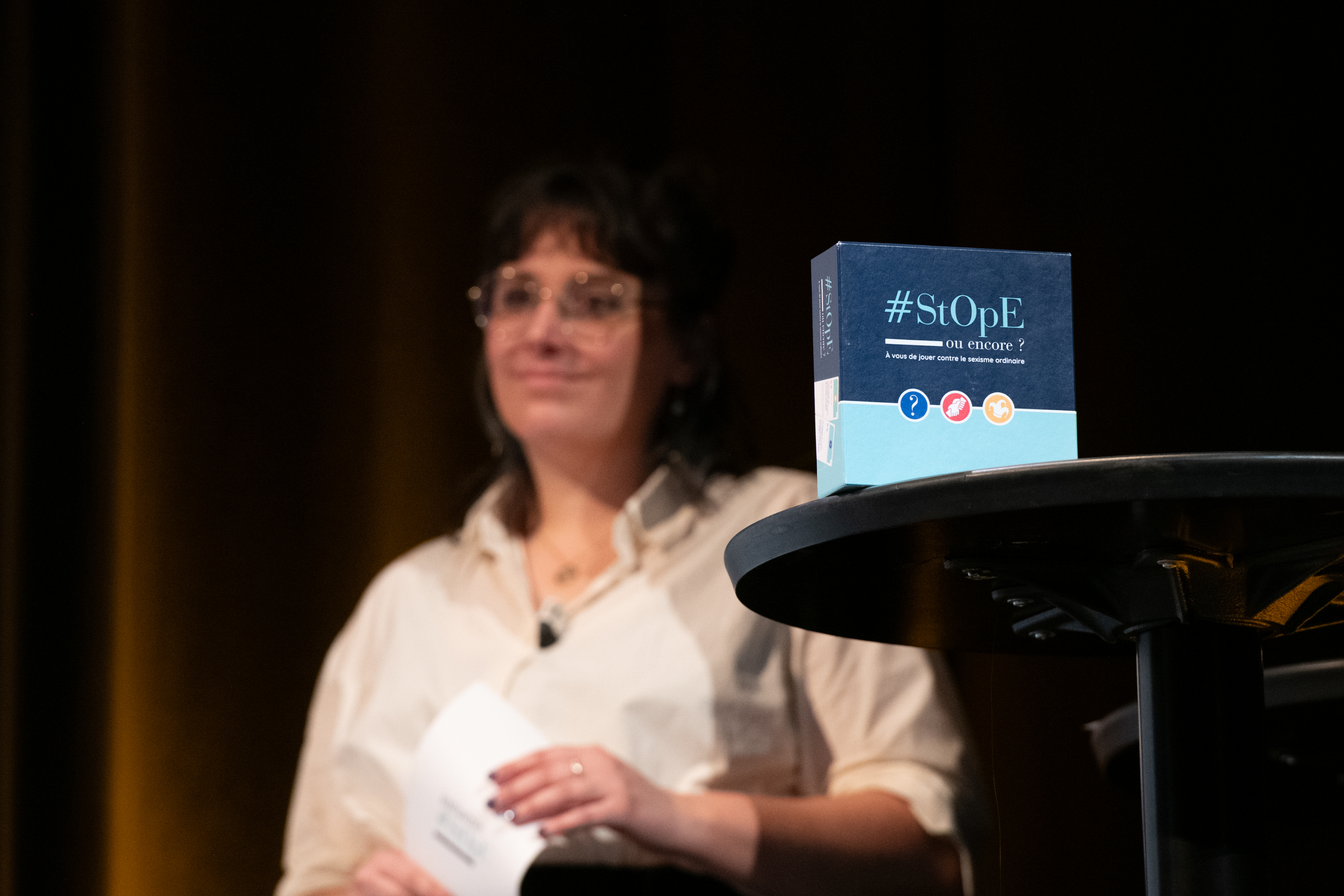 Photo avec le jeu de cartes "#StOpE ou encore?" en avant et Chloé Torcol, maitresse de cérémonie, en fond